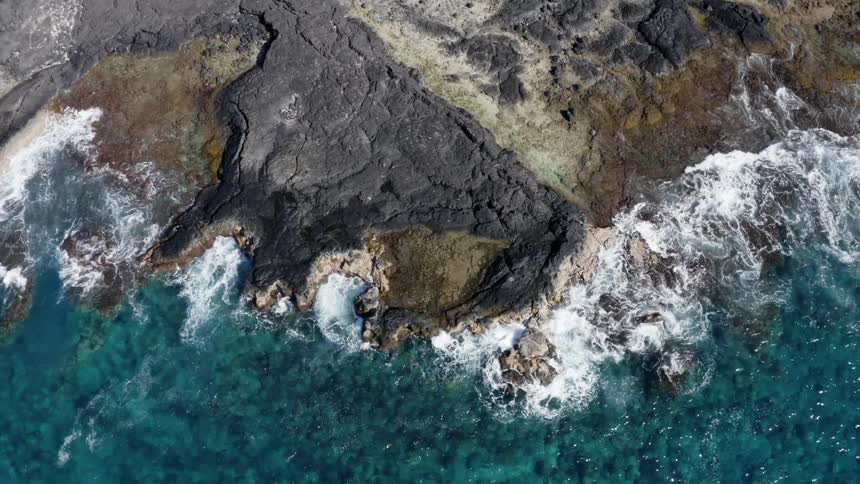 Waves on bright blue ocean crash against low cliff