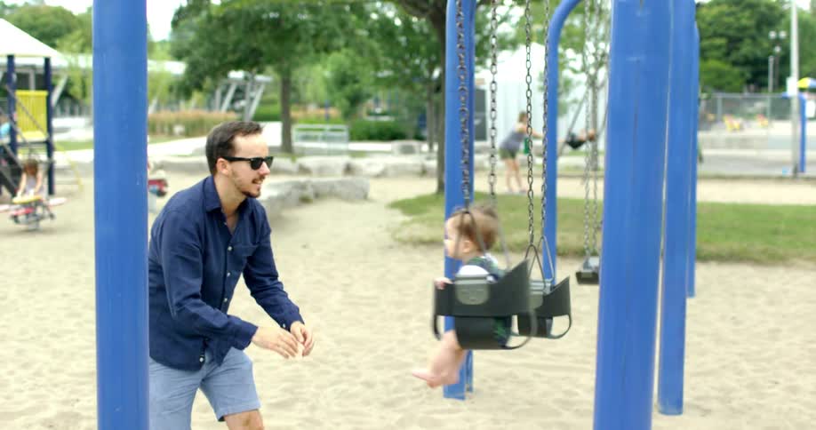 A father pushes his child in a swing at a playground