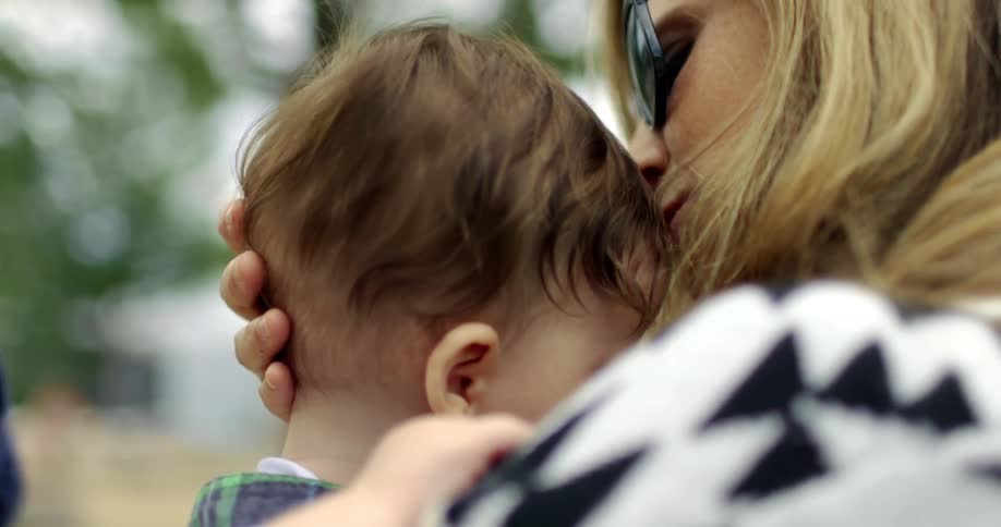 Mother holds and kisses son while father takes pictures with smartphone