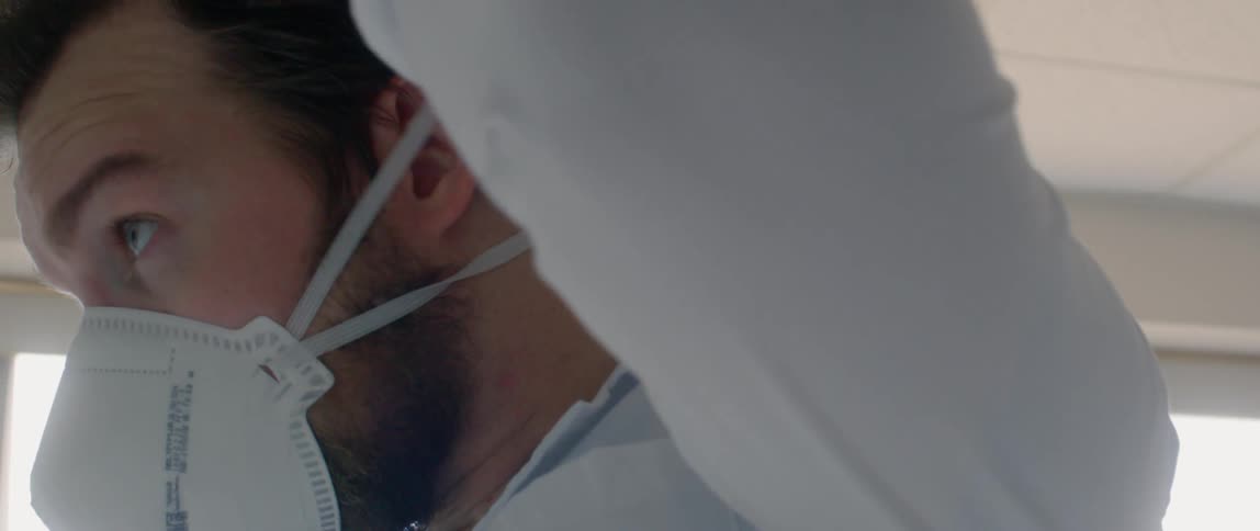 Male puts elastic band of the face mask over his head and adjusts the straps for a proper fit