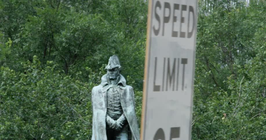Statue sits in front of some trees while a speed limit sign stands nearby