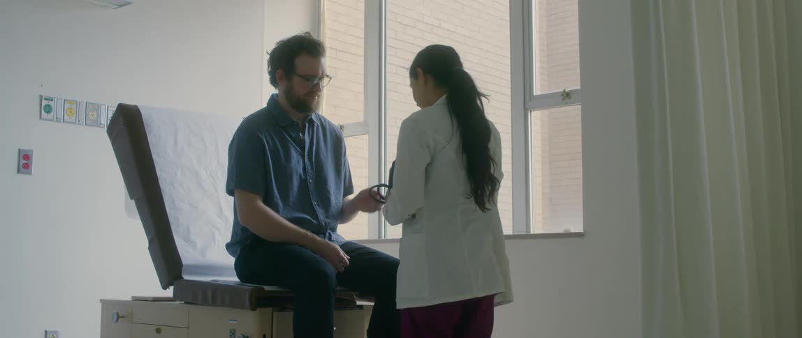 A female doctor walks into a room and puts a blood pressure cuff on a male patient