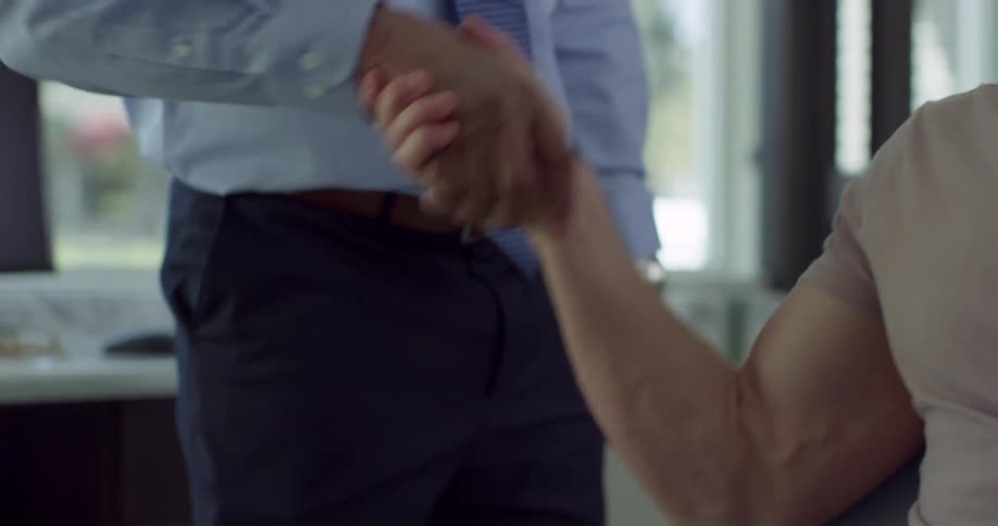 A man walks in to an office and shakes another mans hand