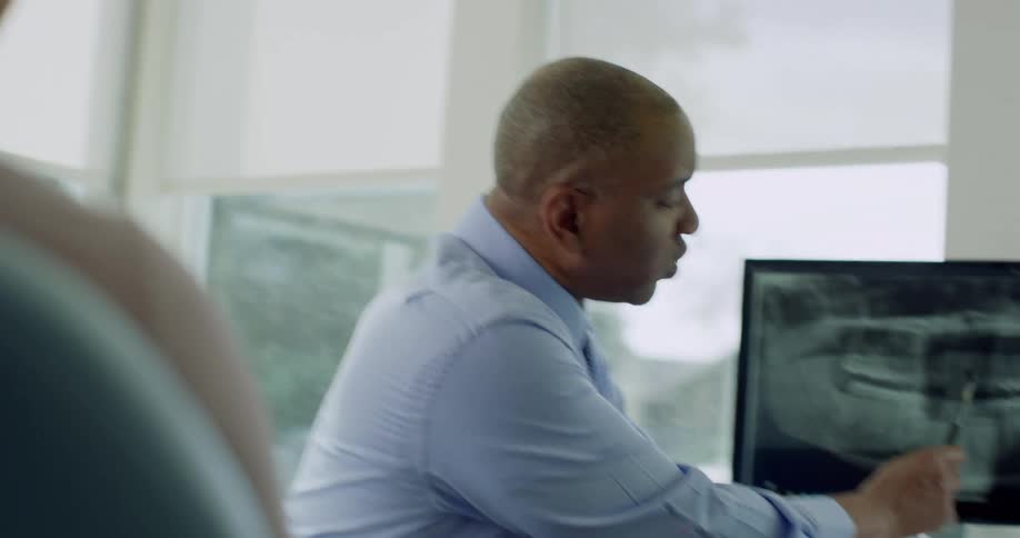 A dentist shows a patient an x ray image on a monitor in his office