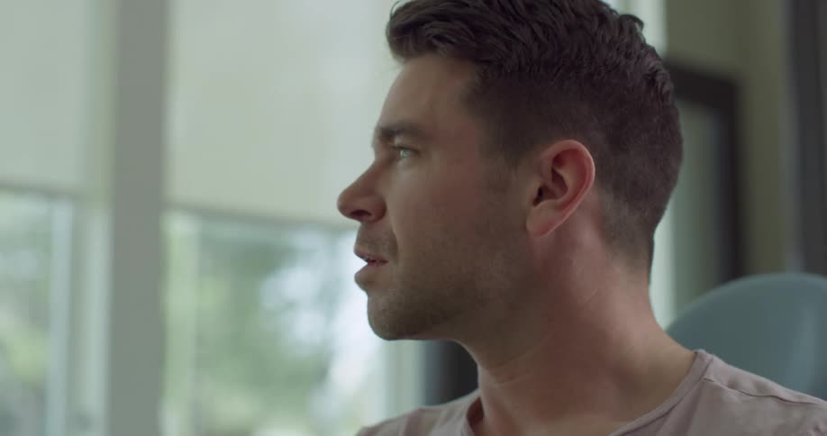A man wearing a tee shirt sits in an office having a conversation with another man wearing a shirt and tie
