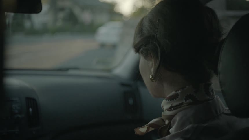 A woman speaking and smiling from the passenger seat of a vehicle as it travels down the road