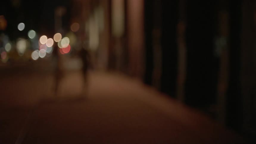 A man and woman sprint down a city sidewalk at night