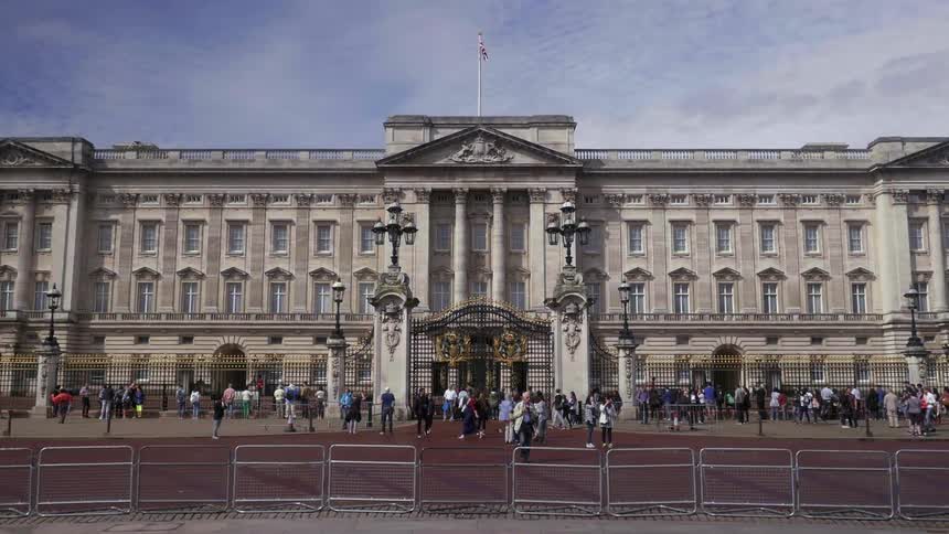 A crowd of people are standing and walking in front of Buckingham Palace