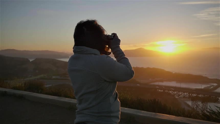 A woman raises her camera to photograph the sunset
