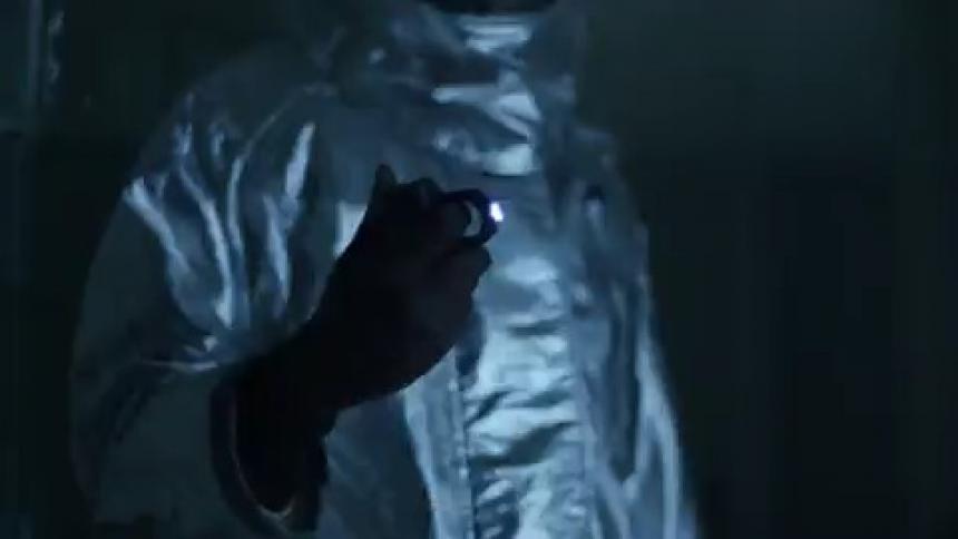 A person in a hazmat suit is searching around the hall with flashing lights
