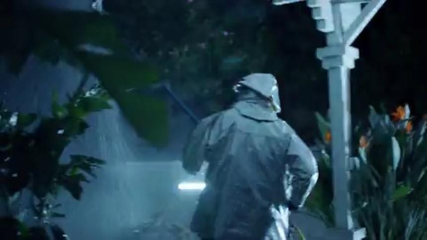 Pedestrian wearing a raincoat walks outdoors while lightning flashes
