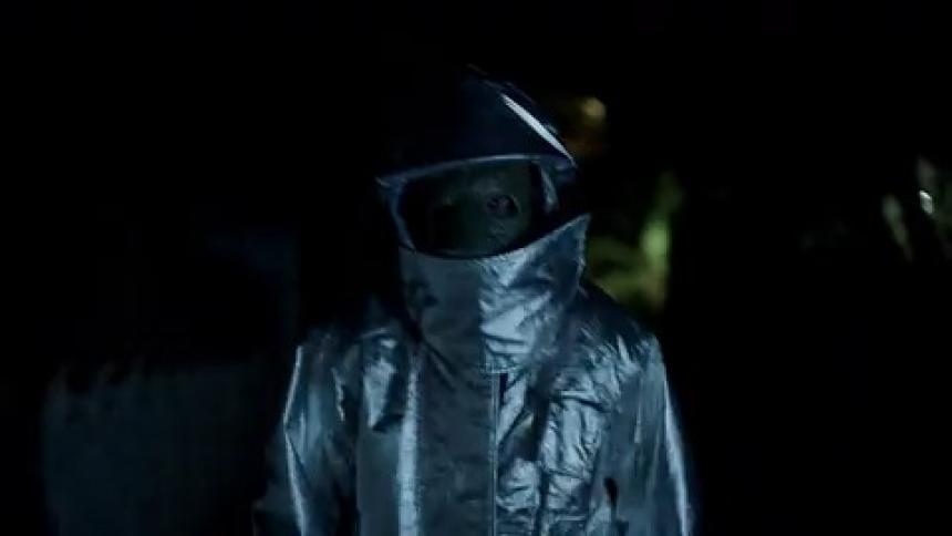 Lights flash as a man in a reflective silver suit and helmet walks down a path