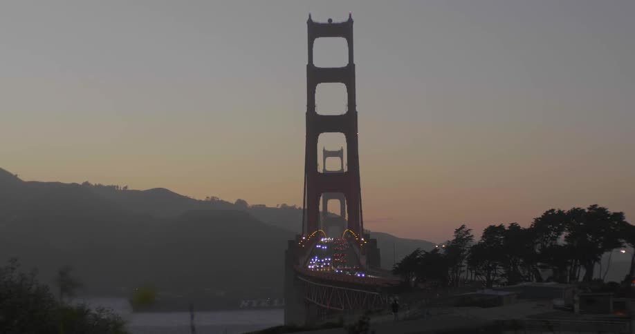 Vehicles can be seen in the distance driving over a bridge at sunset