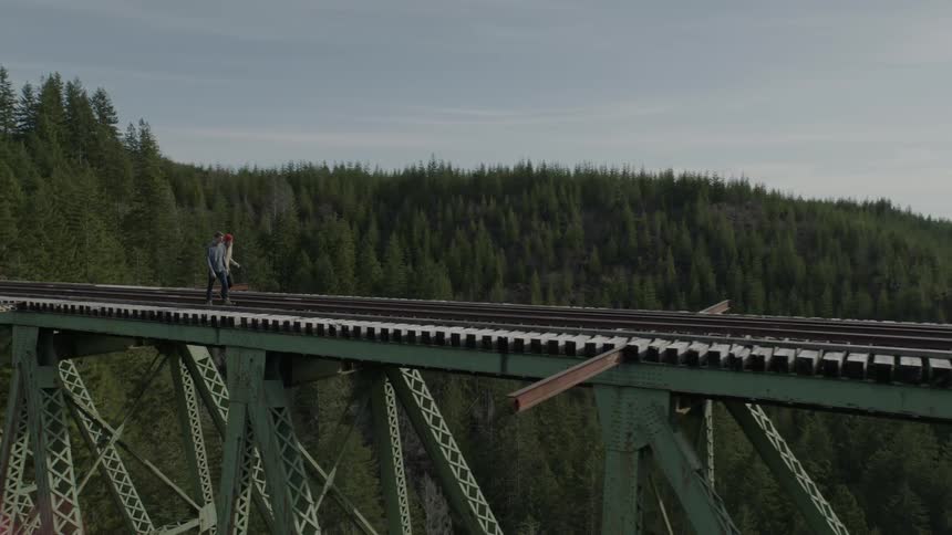 Two people are walking along train tracks on a bridge