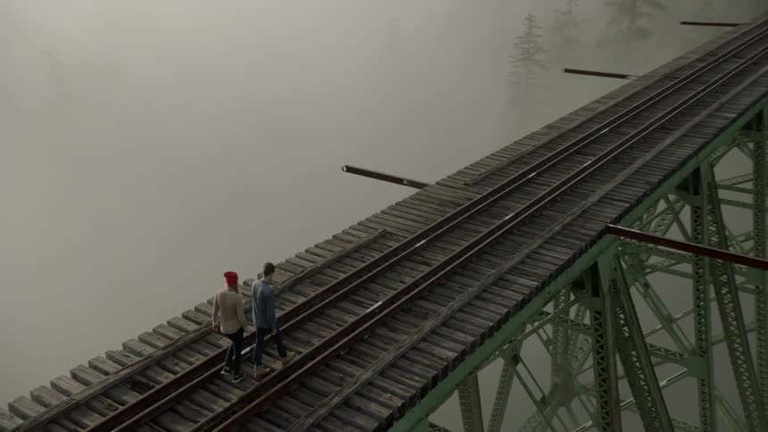 People are walking across a bridge with train tracks on a foggy day