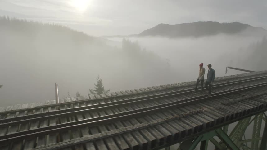 Two people walking across a high bridge over a foggy forest