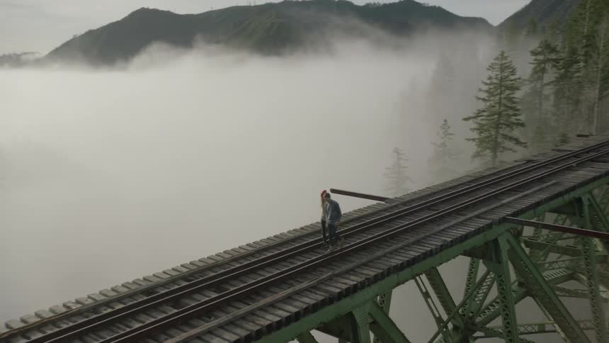 Two people are walking across a train bridge on a foggy day