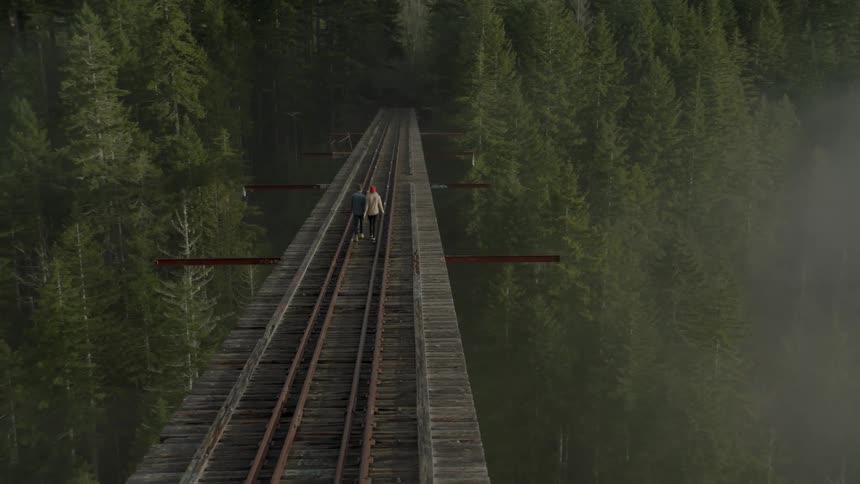 Two people walk on a large railroad bridge