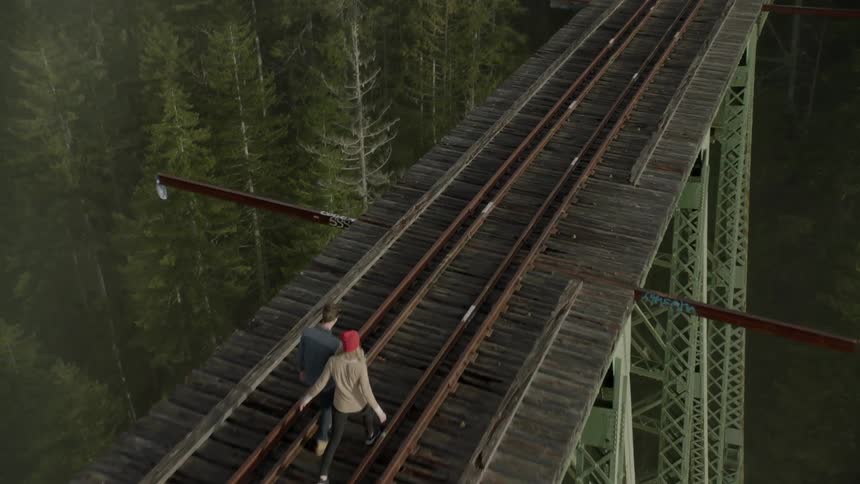 Two people are walking along the tracks on a bridge