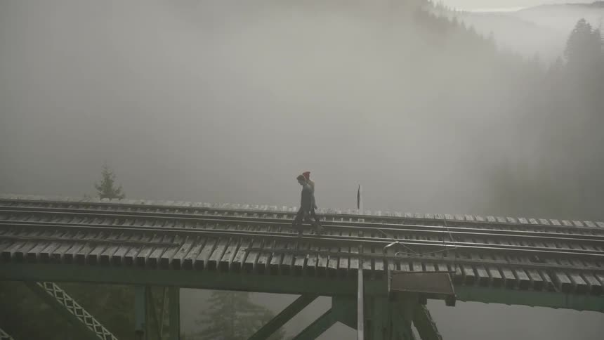 Two people are walking along the tracks on a bridge on a foggy day