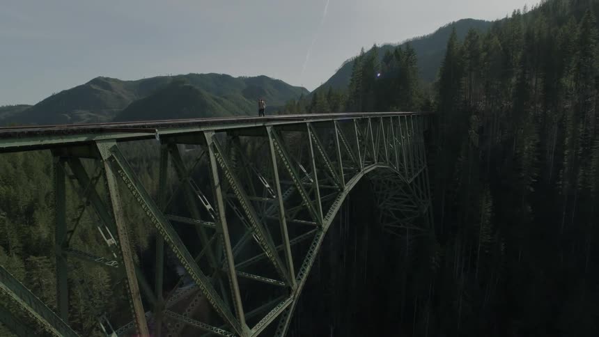 People walking across a train trestle that spans a mountain canyon