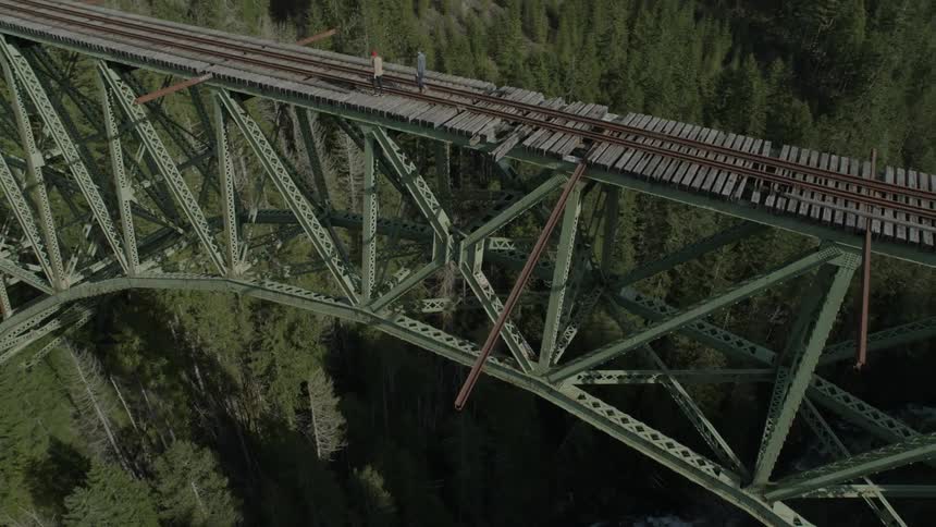 People walking across a train trestle that spans a mountain canyon