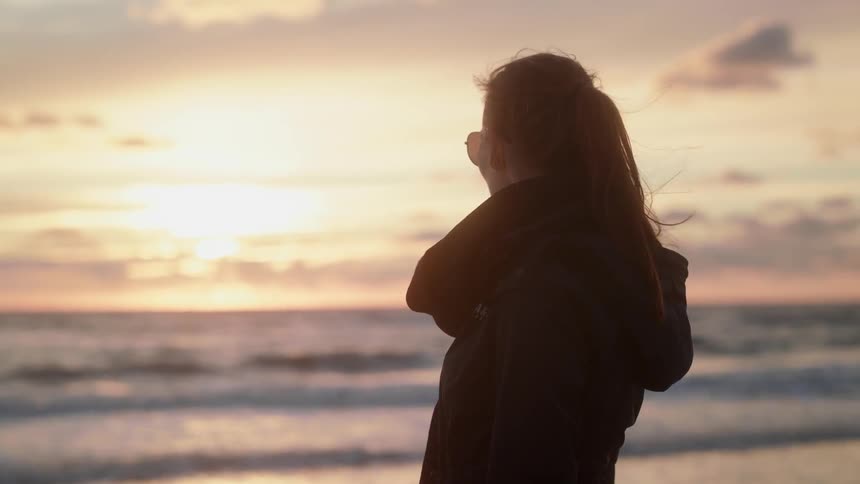 A woman stands staring out at the ocean