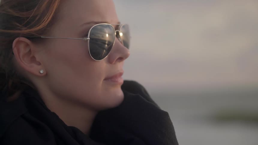 A woman, wearing sunglasses and gazing out at the horizon on a windy day