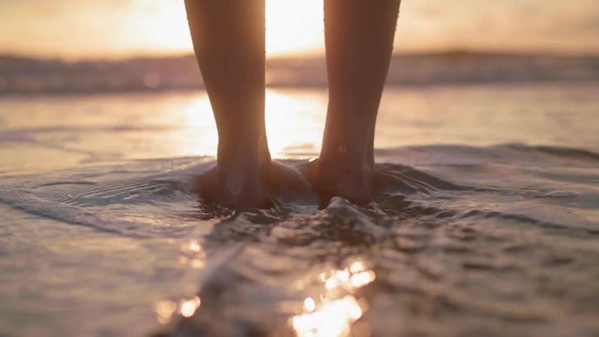 A person stands in the surf at sunset
