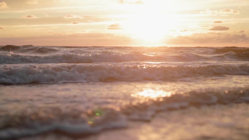 Waves are moving across the water at sunset