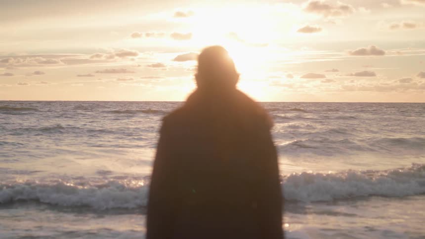A person is standing by the shore watching the sun set