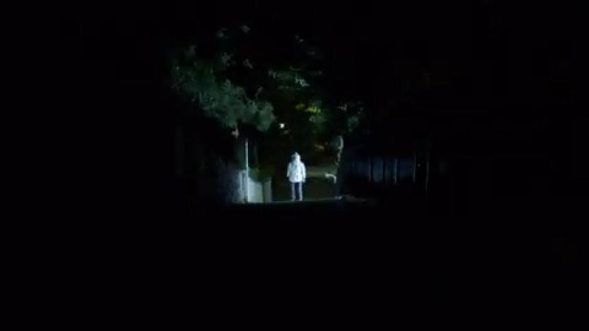 A man stands at the end of a walkway with his head covered in a thick silver coat as lights flash around him