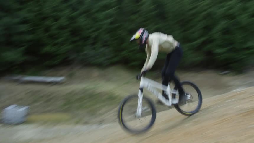 A person rides a bicycle in a tree filled rural area and does an aerial jump over a dirt pile