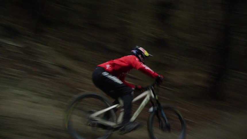 Bike rider races along forest path jumping down incline