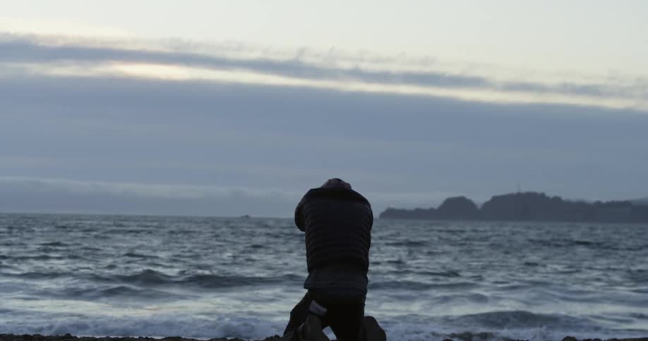 A man falls onto his knees crying at the edge of the ocean