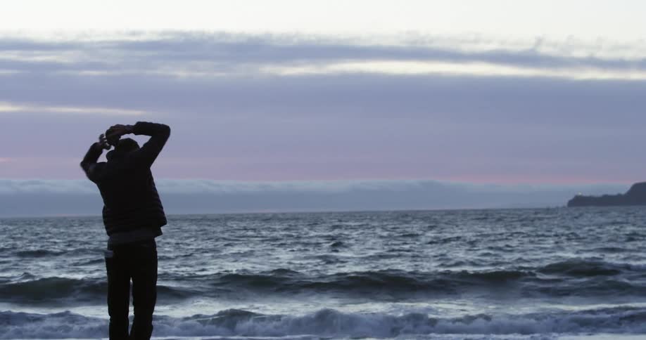 Angry male walking towards shoreline at dusk then kneeling down crying in distress