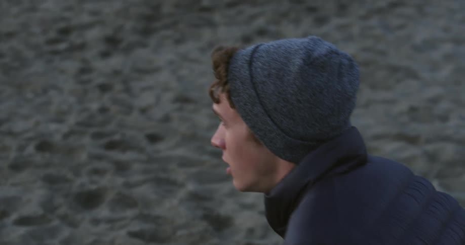 A man looking distraught drops to his knees on a riverside beach
