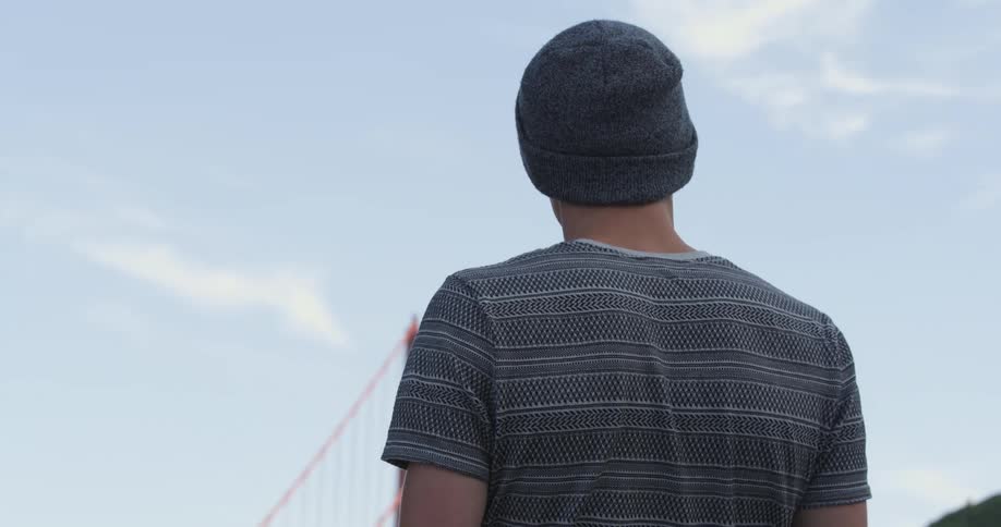 Man with a grey beanie and t shirt stands and watches golden gate bridge
