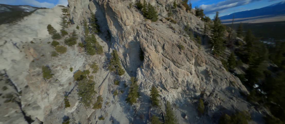 Aerial view of mountain peak with pine trees surrounded by valleys and mountain ranges