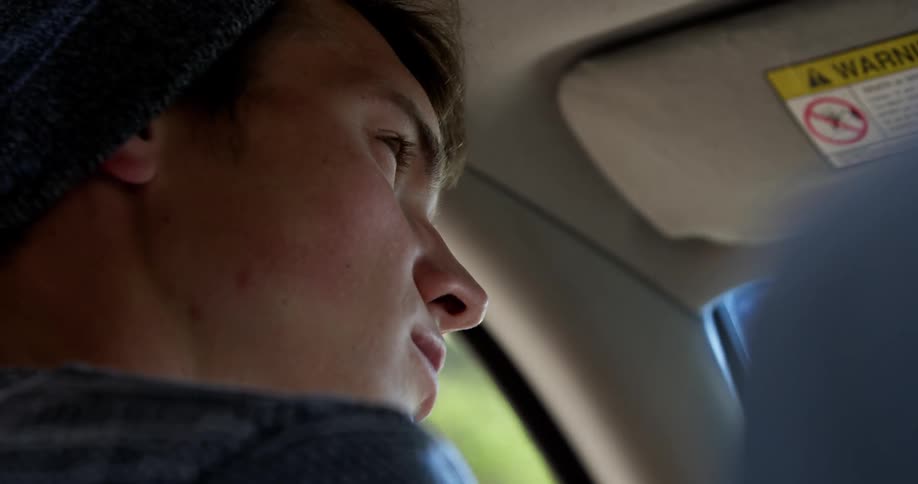 A young man sitting in the front seat of a moving car
