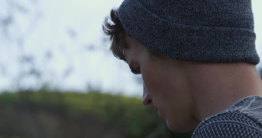 Man with grey beanie hangs his head and then raises it on a windy day