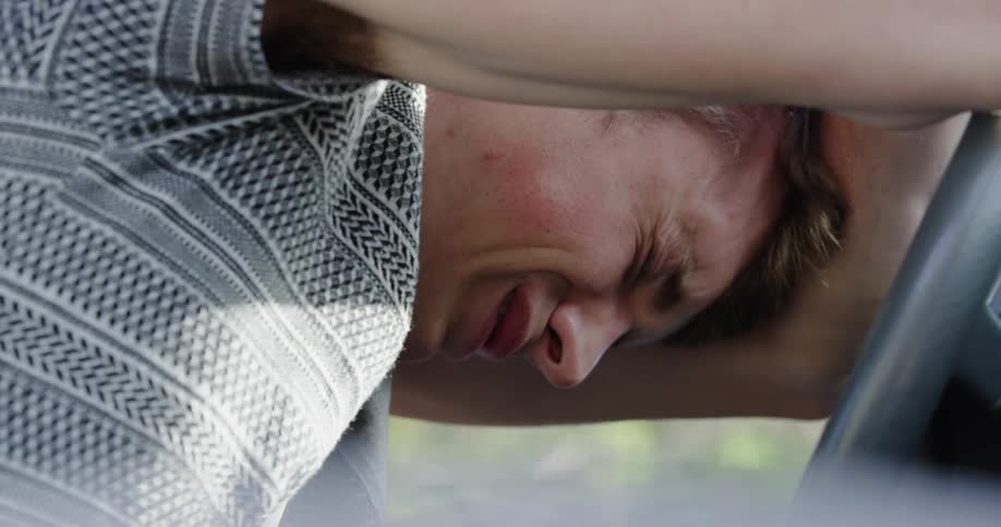 A teenager leans against a steering wheel and cries