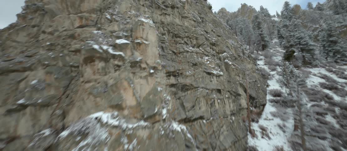 A rocky ridge of a mountain covered in trees and patchy snow