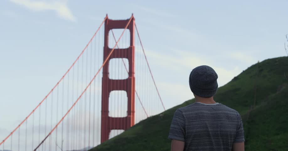 Male standing completely still at the bottom of a hill stares at the golden gate bridge