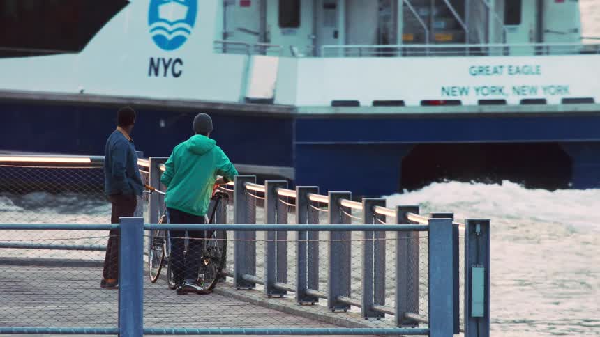 Two men stand on a pier watching a passenger ship pass nearby in the evening