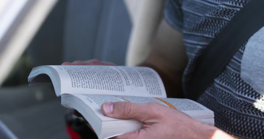 Man sitting on front seat of a car reads a book