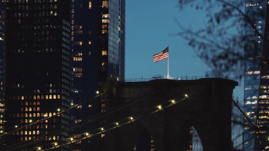 An american flag waving in the wind atop a bridge in a metropolis at night