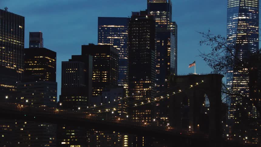 The american flag flies above a city bridge with city skyline behind at night