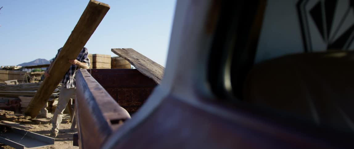 A man lifts a large piece of wood and places it in the bed of his truck