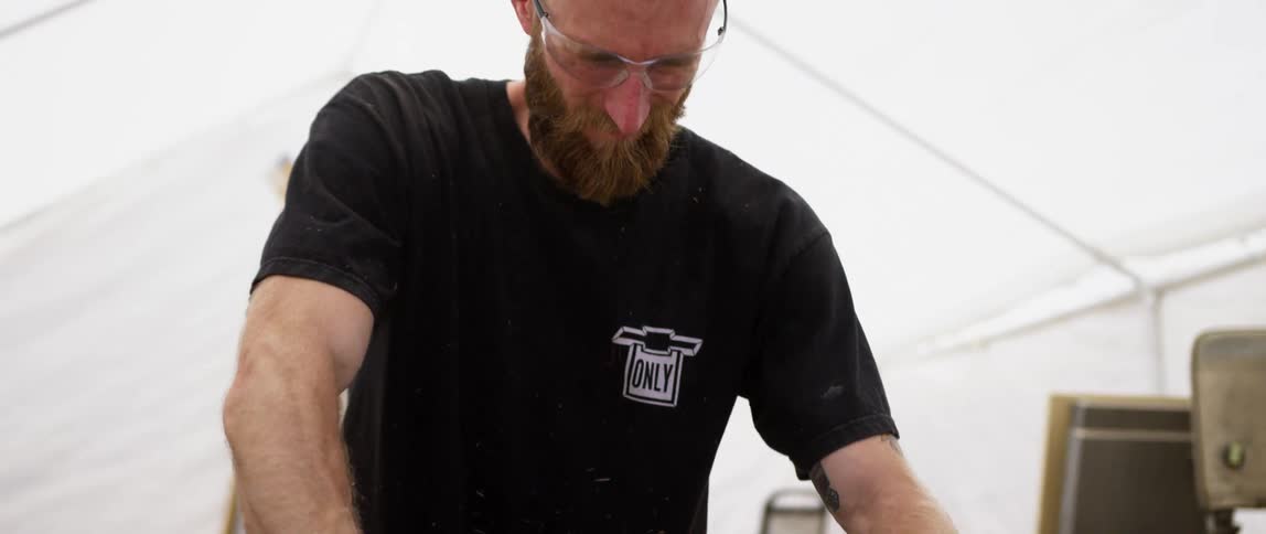A man is cutting a piece of wood in the tent